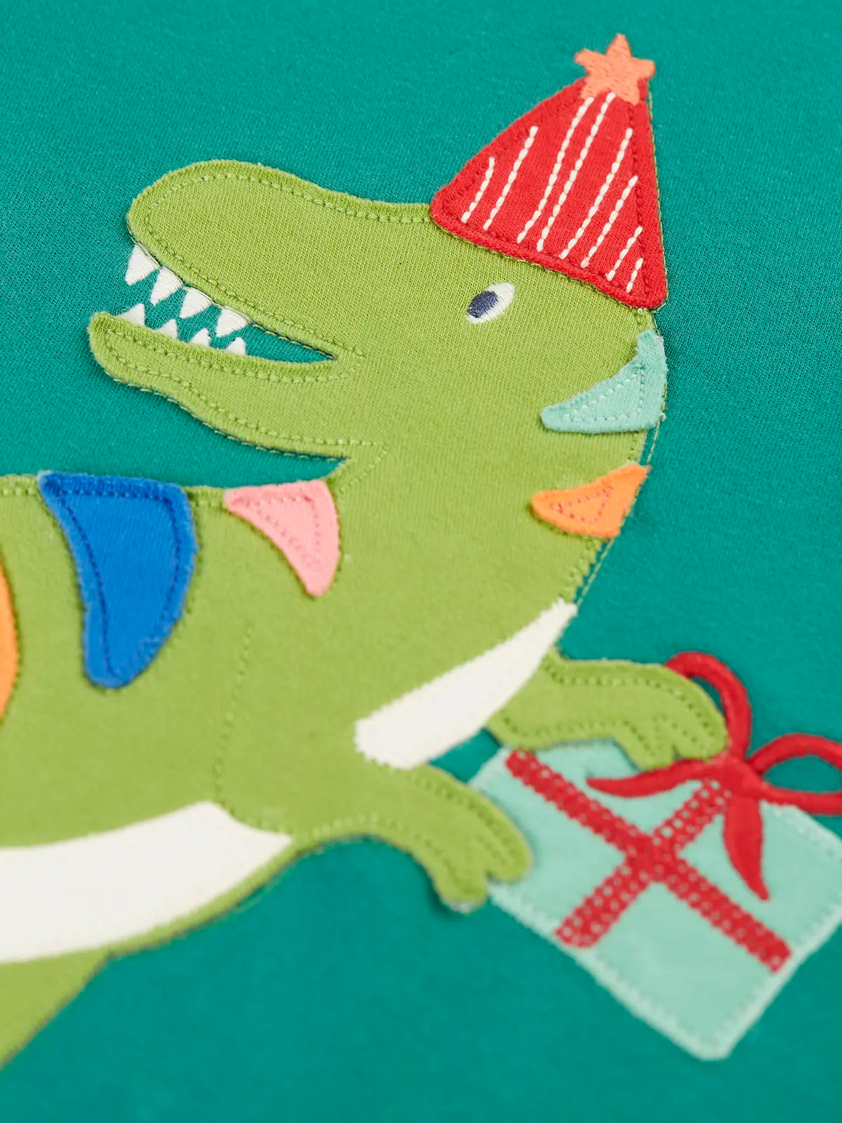 Close up of the green t-rex dinosaur applique on the Frugi organic cotton adventure long sleeve hut green child's top.