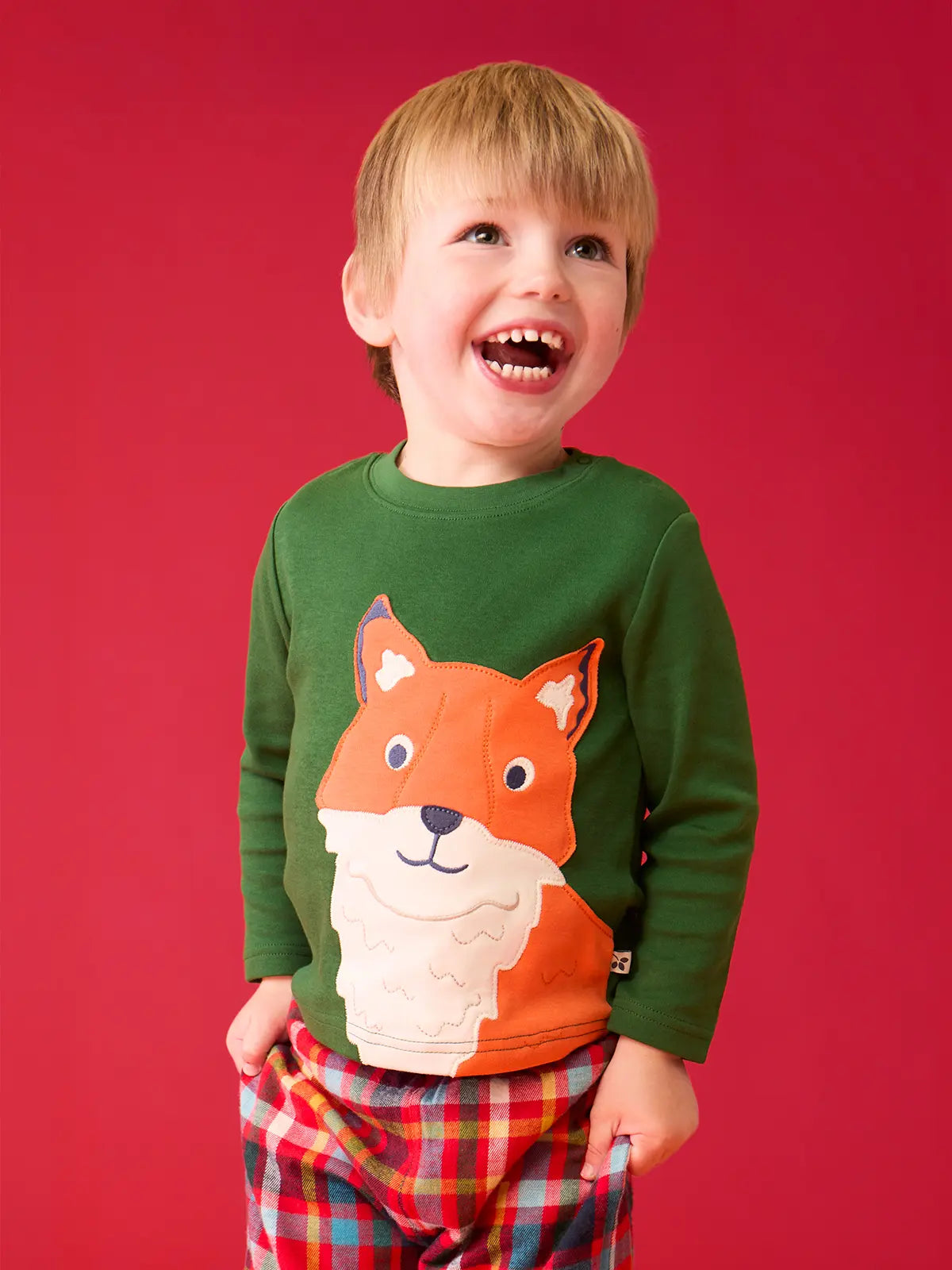 Child wearing the Frugi organic cotton adventure long sleeve top in forest green with large fox applique on the front with festive check trousers.