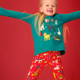 Child wearing the Frugi organic cotton anna pet Paw-Ty appliqué long sleeve children's top with red matching print leggings. Green top with applique dogs, guinea pig, budgie, goose and tortoise wearing party hats and balloons and star sparkle details. 