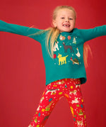 Child wearing the Frugi organic cotton anna pet Paw-Ty appliqué long sleeve children's top with red matching print leggings. Green top with applique dogs, guinea pig, budgie, goose and tortoise wearing party hats and balloons and star sparkle details. 