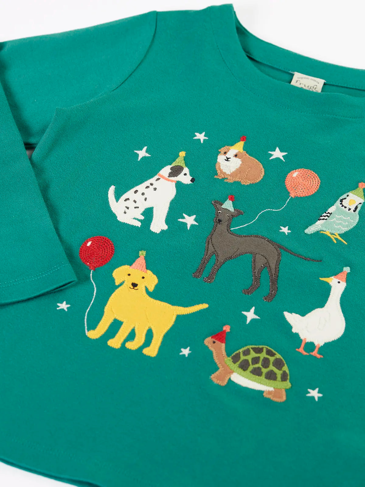 Close up of the Frugi organic cotton anna pet Paw-Ty appliqué long sleeve children's top. Green top with applique dogs, guinea pig, budgie, goose and tortoise wearing party hats and balloons and star sparkle details. 