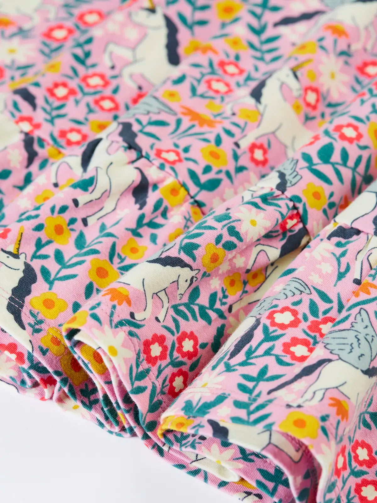Close up of the front of the Frugi organic cotton annika skater dress with floral flight print and frilled shoulders. All over print featuring pegasus, flowers and foliage. 