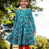 Child wearing the Frugi organic cotton annika skater dress with winter drives print. All over print featuring houses, campers, snow topped mountains, snowman and trees in a festive scene. 