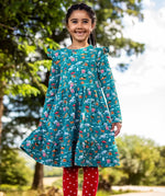 Child wearing the Frugi organic cotton annika skater dress with winter drives print. All over print featuring houses, campers, snow topped mountains, snowman and trees in a festive scene. 