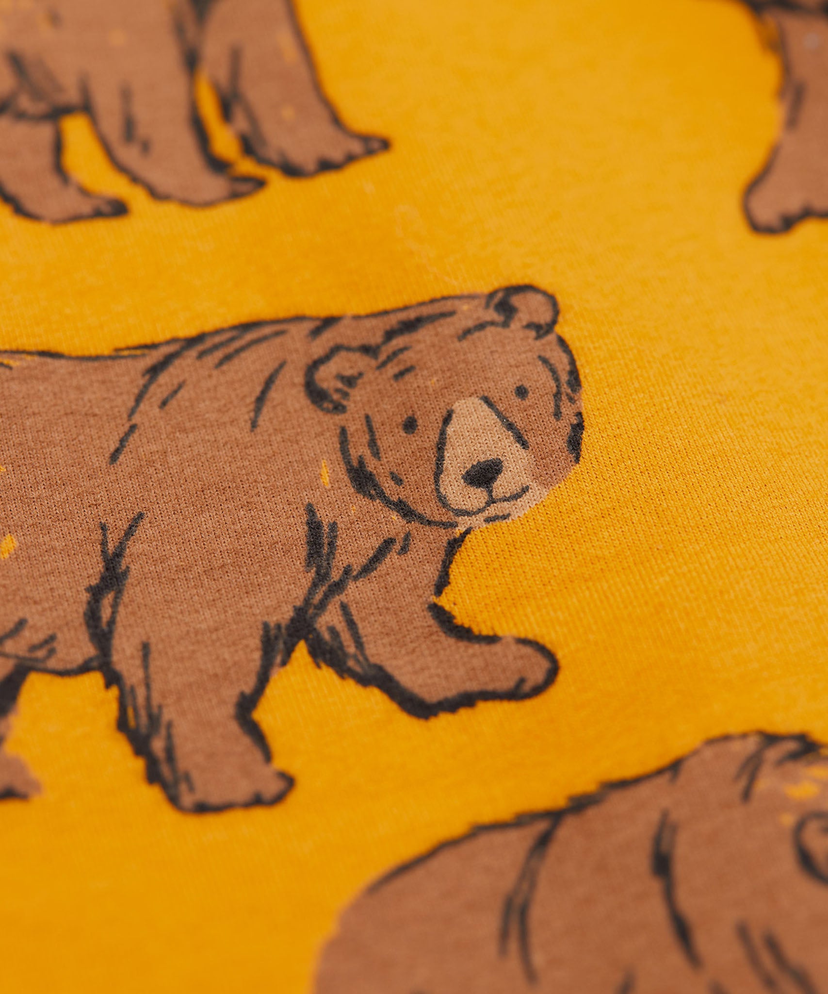 A close up of the Frugi kids beary wild parsnip joggers showing the bear print detail on dark yellow organic cotton fabric.