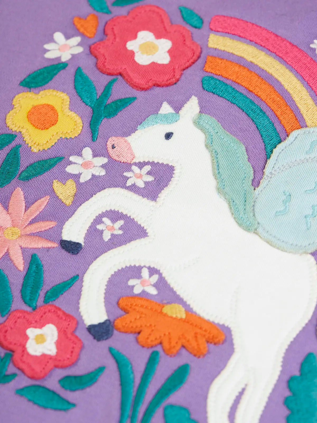 Pegasus applique with a rainbow and flowers applique on the front of the Frugi organic cotton bethany long sleeved periwinkle purple top.