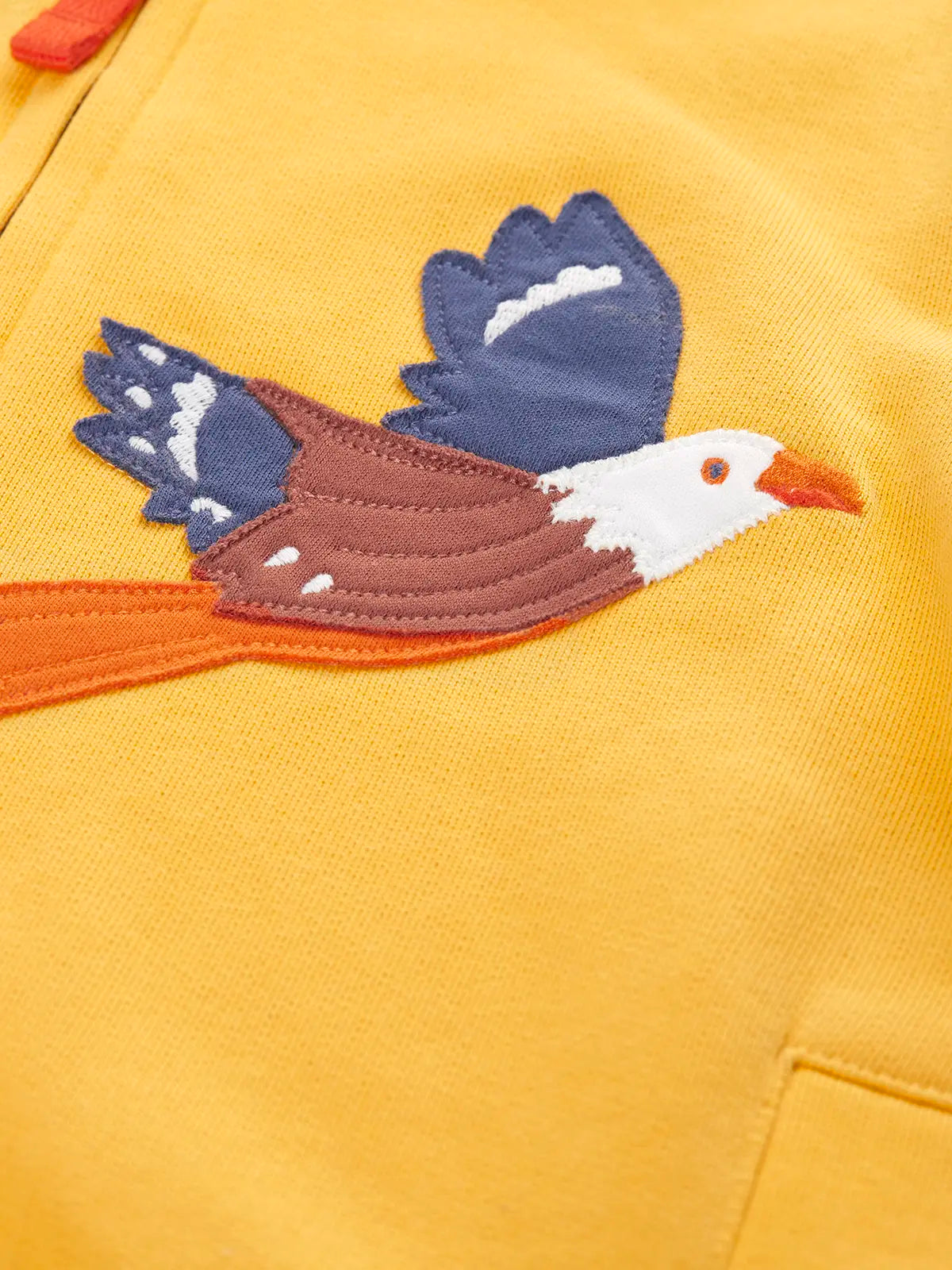 Close up of the eagle applique on the Frugi organic cotton blaire zip hoodie in bumblebee yellow. 