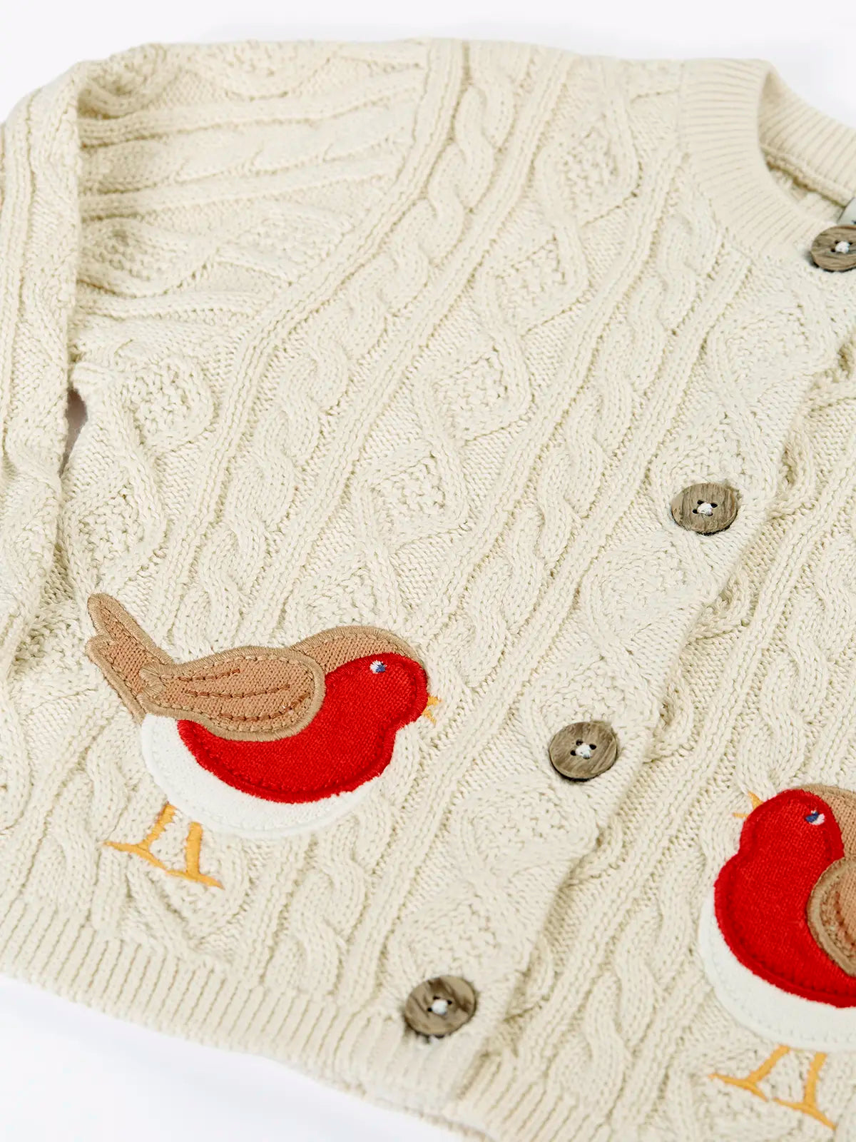 Close up of the Frugi organic cotton natural cream cable knit baby cardigan with robin appliques.