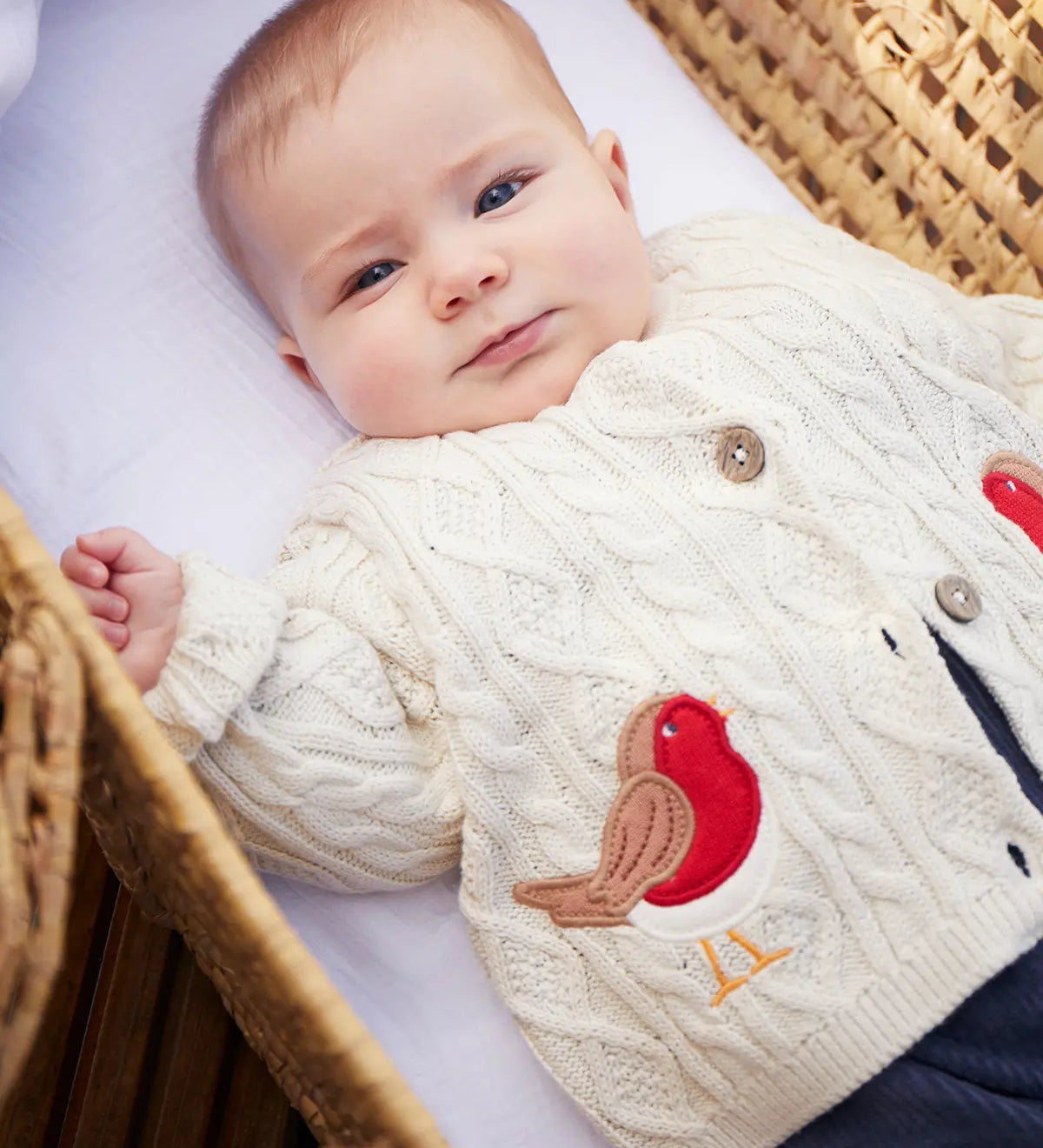 Baby wearing the Frugi organic cotton natural cream cable knit baby cardigan with a robin applique on each side.