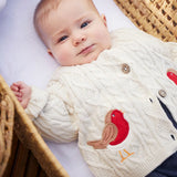 Baby wearing the Frugi organic cotton natural cream cable knit baby cardigan with a robin applique on each side.