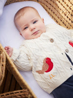 Baby wearing the Frugi organic cotton natural cream cable knit baby cardigan with a robin applique on each side.