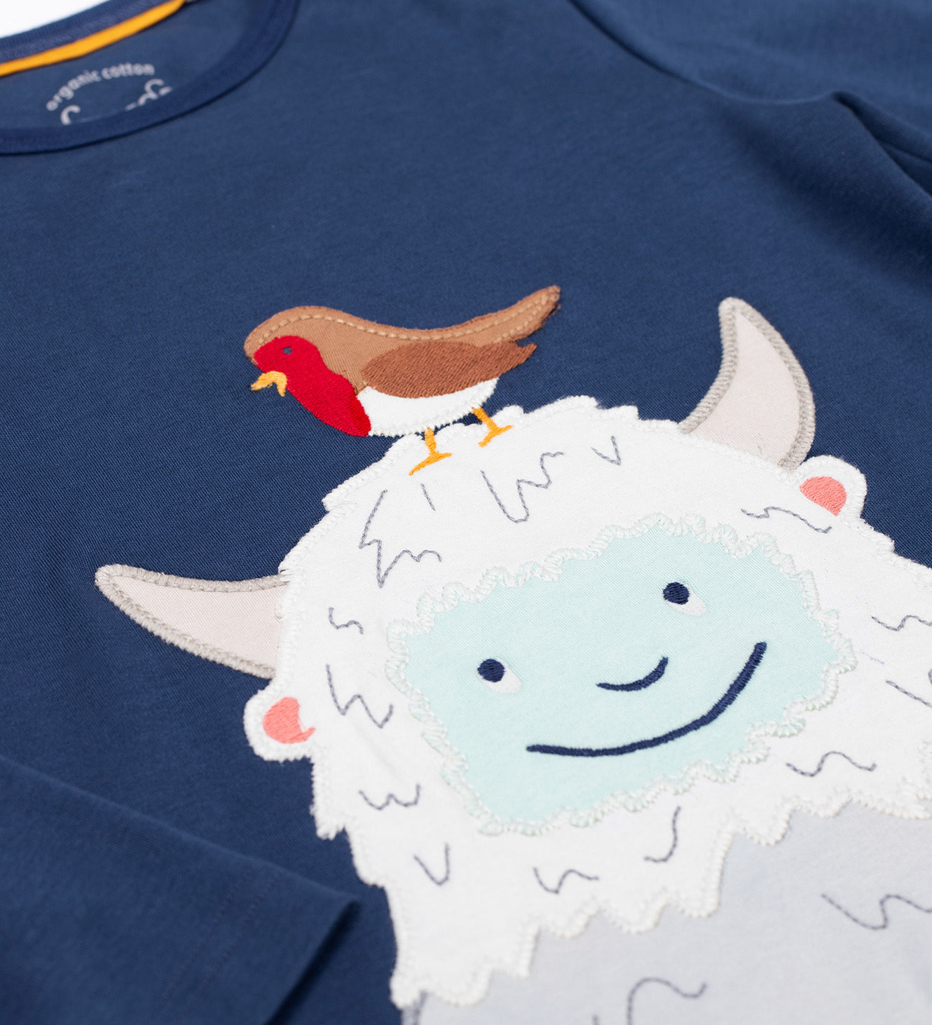 A close up of the white yeti applique on the front of the top from the Frugi Organic Cotton Caden Christmas Pyjamas. The yeti has a robin redbreast on it's head. These pyjamas are part of a wide range of organic cotton clothing for children available here at Babipur. 