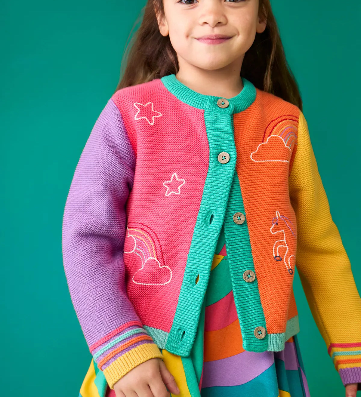 Child wearing the Frugi organic cotton cammie cardigan with a hotchpotch unicorn design. white star, clouds and unicorn outlines details on the front. 