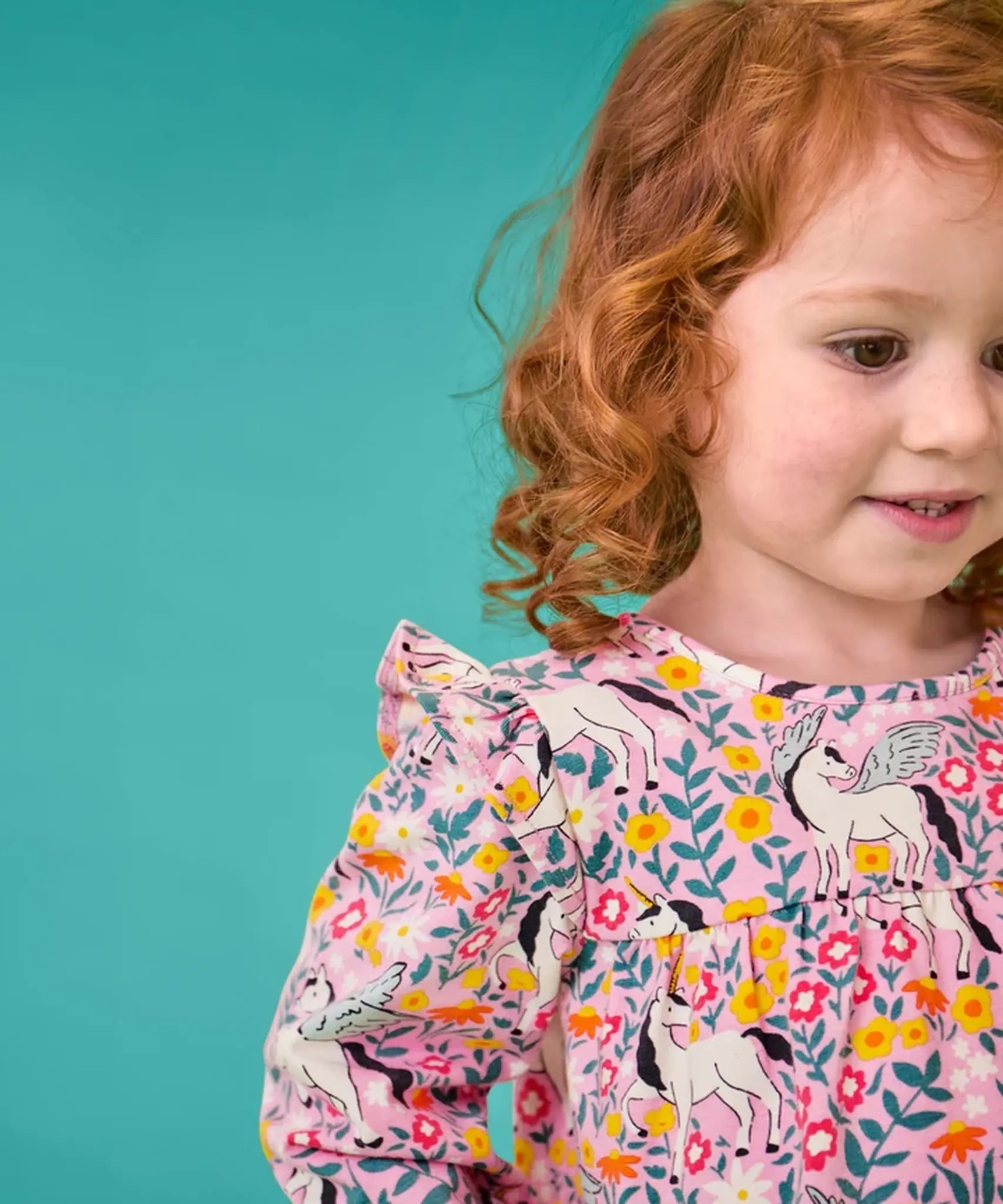 Close up of a frilled shoulders on the top from the Frugi organic cotton Charlotte outfit. All over floral flight, frilled shoulder long sleeve top with rhubarb pink leggings.