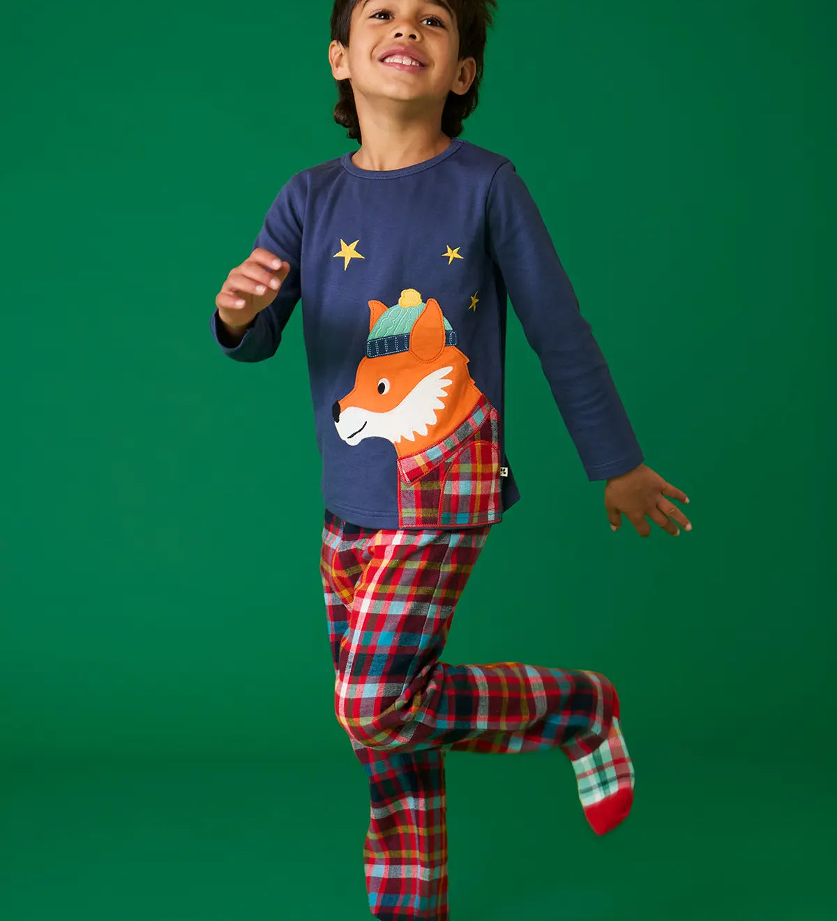 Child wearing the Frugi organic cotton caden check festive fox pyjamas. Long sleeved navy top with fox applique with multi coloured check trousers. 