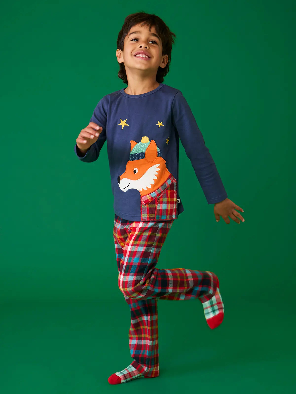 Child wearing the Frugi organic cotton caden check festive fox pyjamas. Long sleeved navy top with fox applique with multi coloured check trousers. 