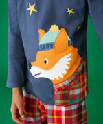 Close up of the fox applique on the long sleeved top from the Frugi organic cotton caden check festive fox pyjamas. The fox is wearing a blue bobble hat and a check shirt.