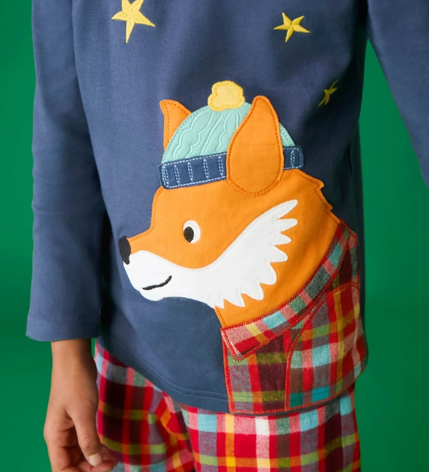 Close up of the fox applique on the long sleeved top from the Frugi organic cotton caden check festive fox pyjamas. The fox is wearing a blue bobble hat and a check shirt.
