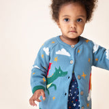 A child wearing the Frugi Organic Cotton Reva Dragon Skies Knitted Kids' Cardigan. This blue cardigan features a fun, colourful design featuring a green dragon, stars, rainbow, clouds and a mushroom. This cardigan is a part of a wide range of organic cotton clothing for children available here at Babipur. 