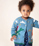 A child wearing the Frugi Organic Cotton Reva Dragon Skies Knitted Kids' Cardigan. This blue cardigan features a fun, colourful design featuring a green dragon, stars, rainbow, clouds and a mushroom. This cardigan is a part of a wide range of organic cotton clothing for children available here at Babipur. 
