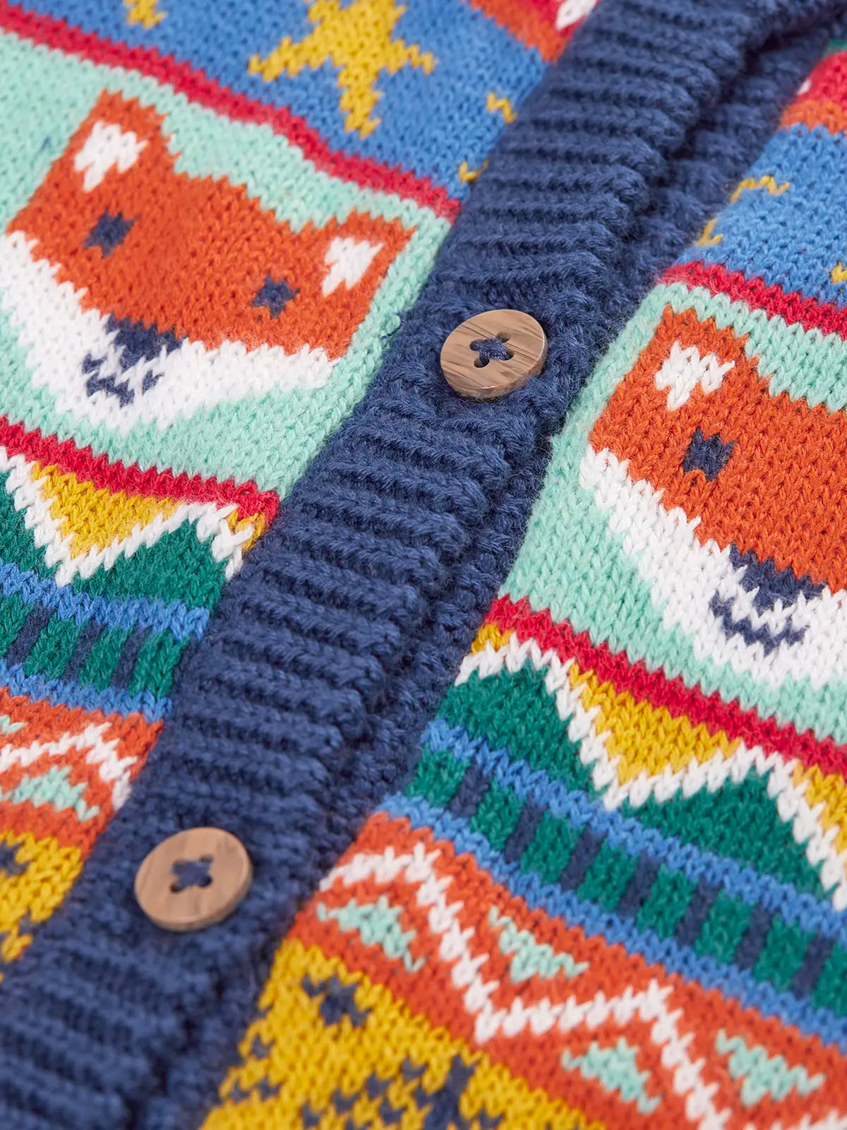 Close up of the wooden buttons on the Frugi fox fair isle organic cotton wenn knitted waistcoat. Multi-coloured fair isle knit with navy edges.