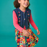 Child wearing the Frugi organic cotton connie navy knitted waistcoat with embroidered flower details, wooden button closure and scalloped edges with a pink long sleeve top underneath and a Marta Twill Skirt with flower stamps design.