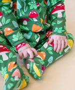 A closeup of a baby's legs and hands, whilst wearing the Frugi organic cotton Lovely Babygrow in a green Fun Guys mushroom print.