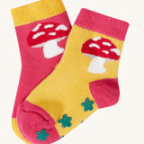 The mushroom design socks from the Frugi kids organic cotton grippy socks 2-pack. The red mushrooms socks features a mushroom design with green flower grips, one sock is yellow one is pink.