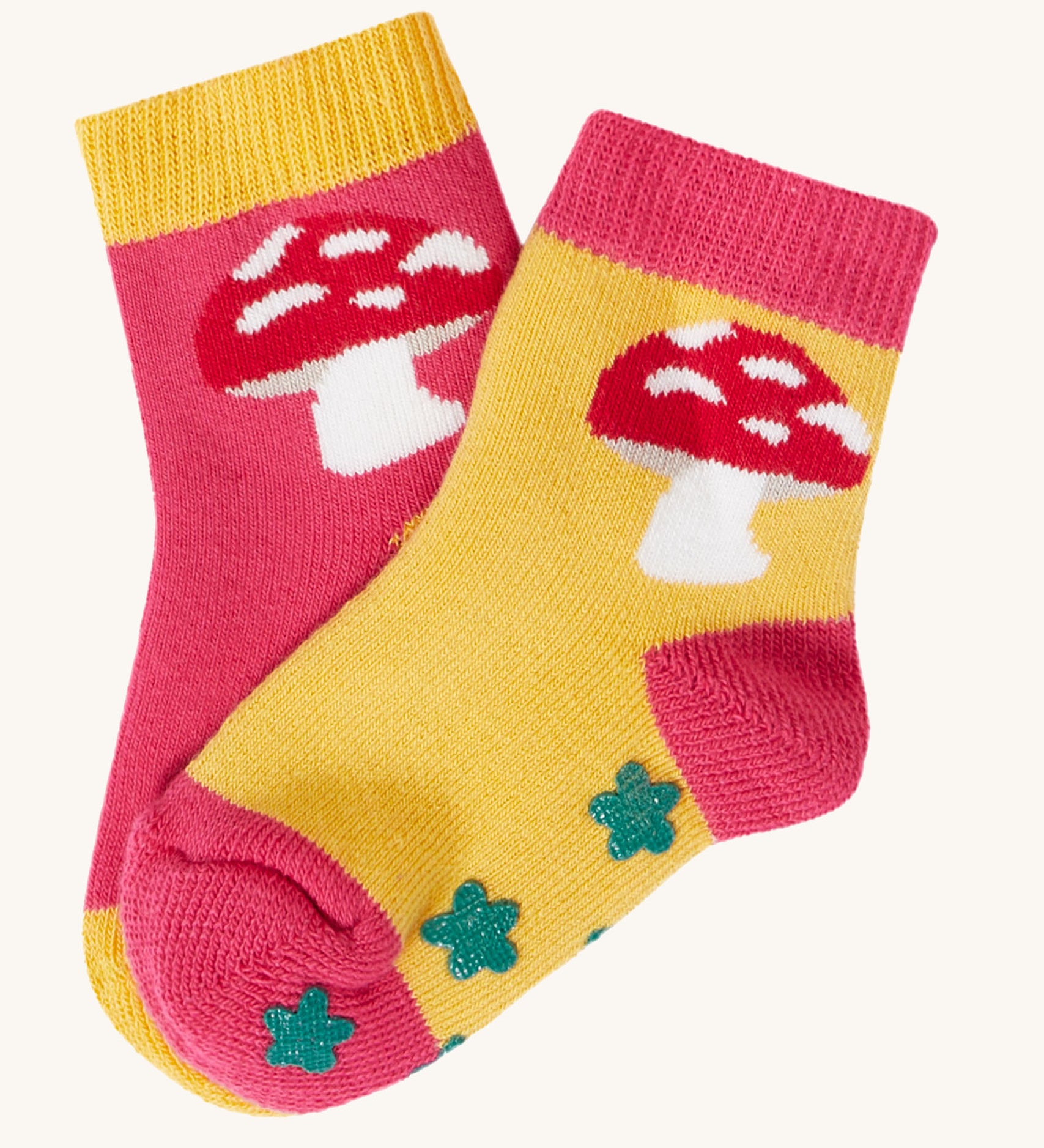 The mushroom design socks from the Frugi kids organic cotton grippy socks 2-pack. The red mushrooms socks features a mushroom design with green flower grips, one sock is yellow one is pink.