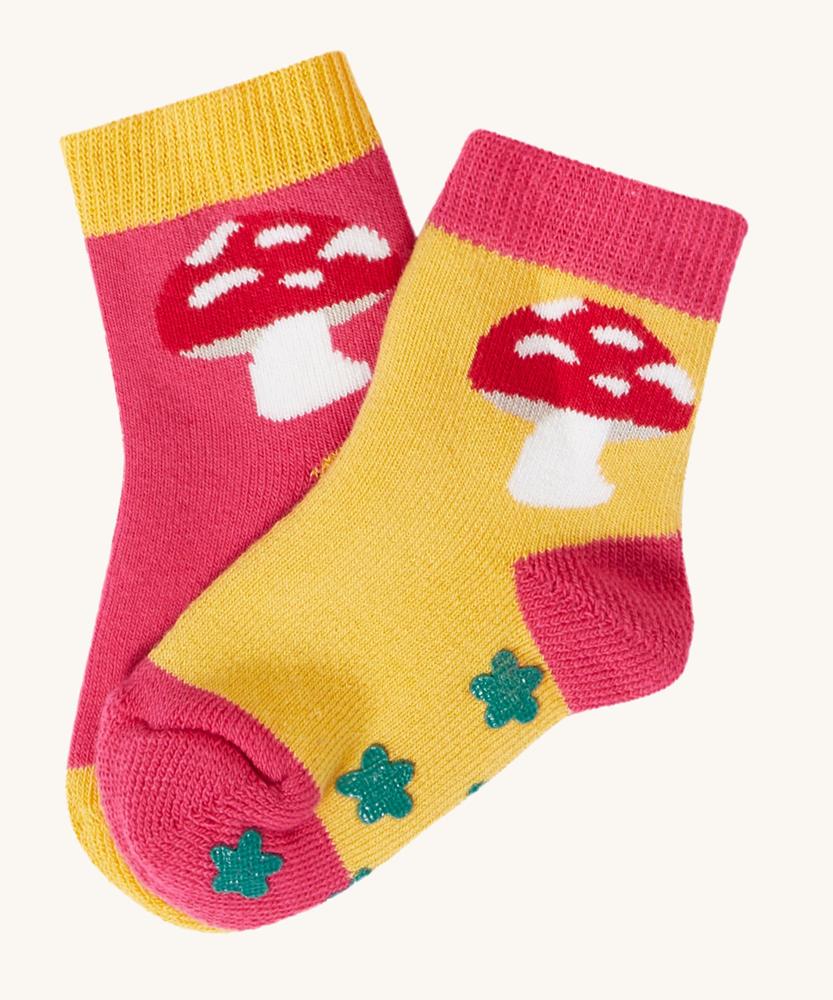 The mushroom design socks from the Frugi kids organic cotton grippy socks 2-pack. The red mushrooms socks features a mushroom design with green flower grips, one sock is yellow one is pink.