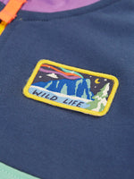 Close up of the rectangle shaped badge on the chest of the Frugi organic cotton half zip sweatshirt hotchpotch wildlife. Yellow edges with a mountainscape with the word wild life in blue underneath.