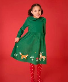 Frugi organic cotton peony corduroy dress in holly green with fox, deer and foliage appliques on the hemline with red spotty tights underneath. 