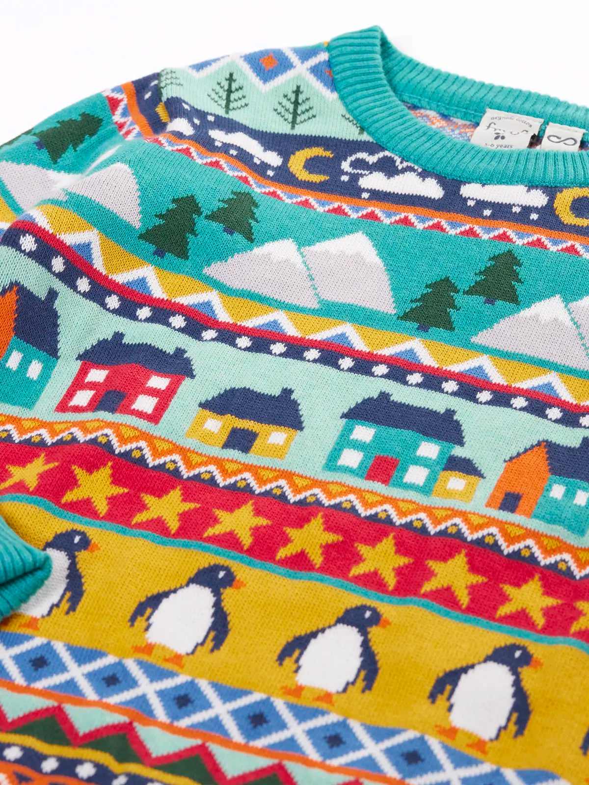 Close up of the patterns on the shoulder of the Frugi festive fair isle organic cotton jumper. Multicoloured fairisle design featuring penguins, stars, houses, mountain, trees, clouds and snowy clouds.