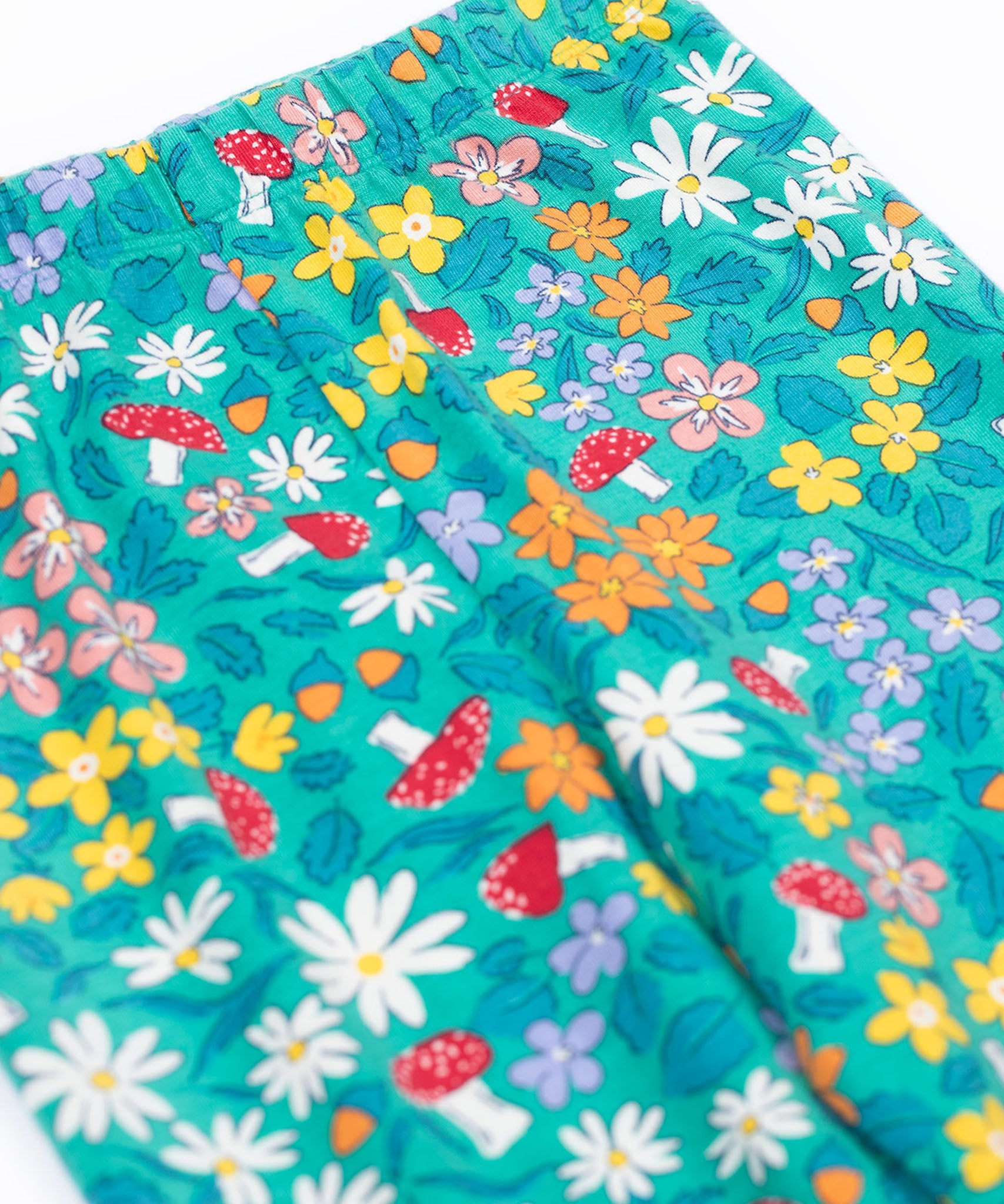 A close up of the Frugi Libby leggings with a wild woods, botanical design on a green background. The leggings have a slim elasticated waist band.