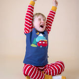 A sleepy child sitting cross legged and stretching his arms ready for bed, wearing the Frugi organic Cotton Jim Jam Pyjamas with a campervan applique design on the front. 