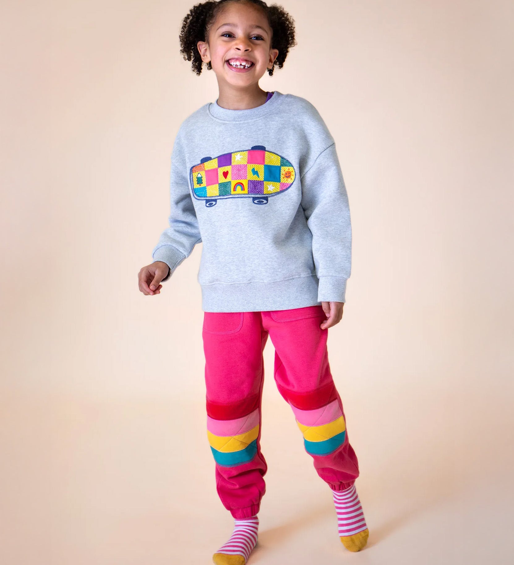 A little girl wearing an organic cotton frugi kids' outfit - an embroidered sweater and pink Malpas joggers.