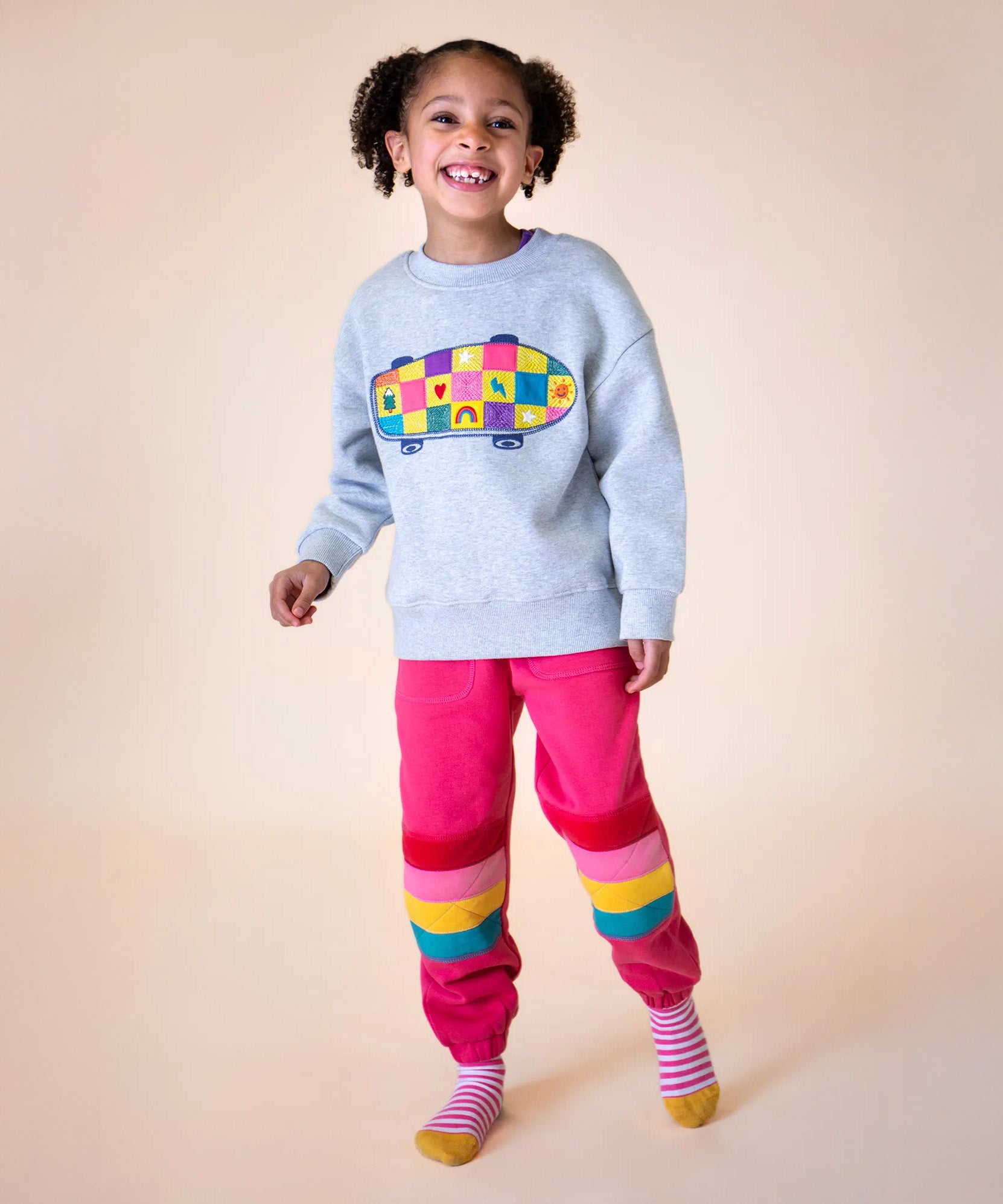 A little girl wearing an organic cotton frugi kids' outfit - an embroidered sweater and pink Malpas joggers.