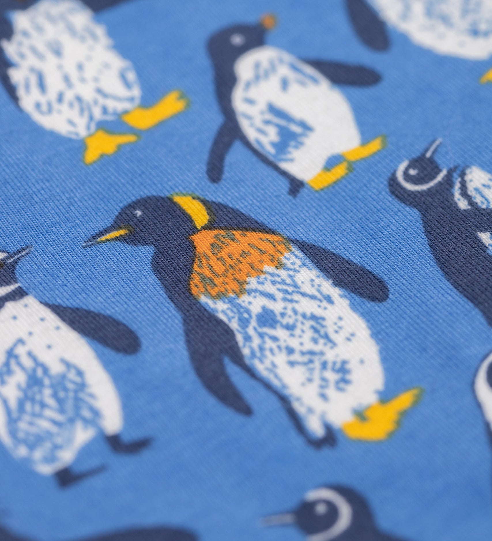 A close up of the print on the Frugi organic cotton kids libby leggings with a penguin waddle print on a blue background.