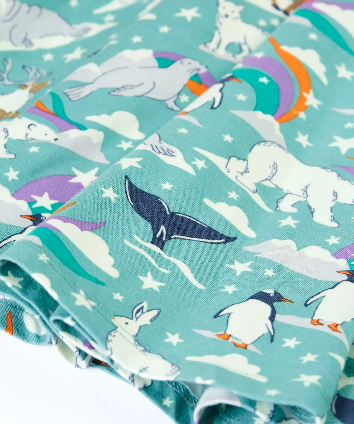 Close up of the print details on the Frugi GOTS organic cotton sofia skater dress in polar aurora. Blue background with and all over print featuring artic animals among star and colourful swishes. 