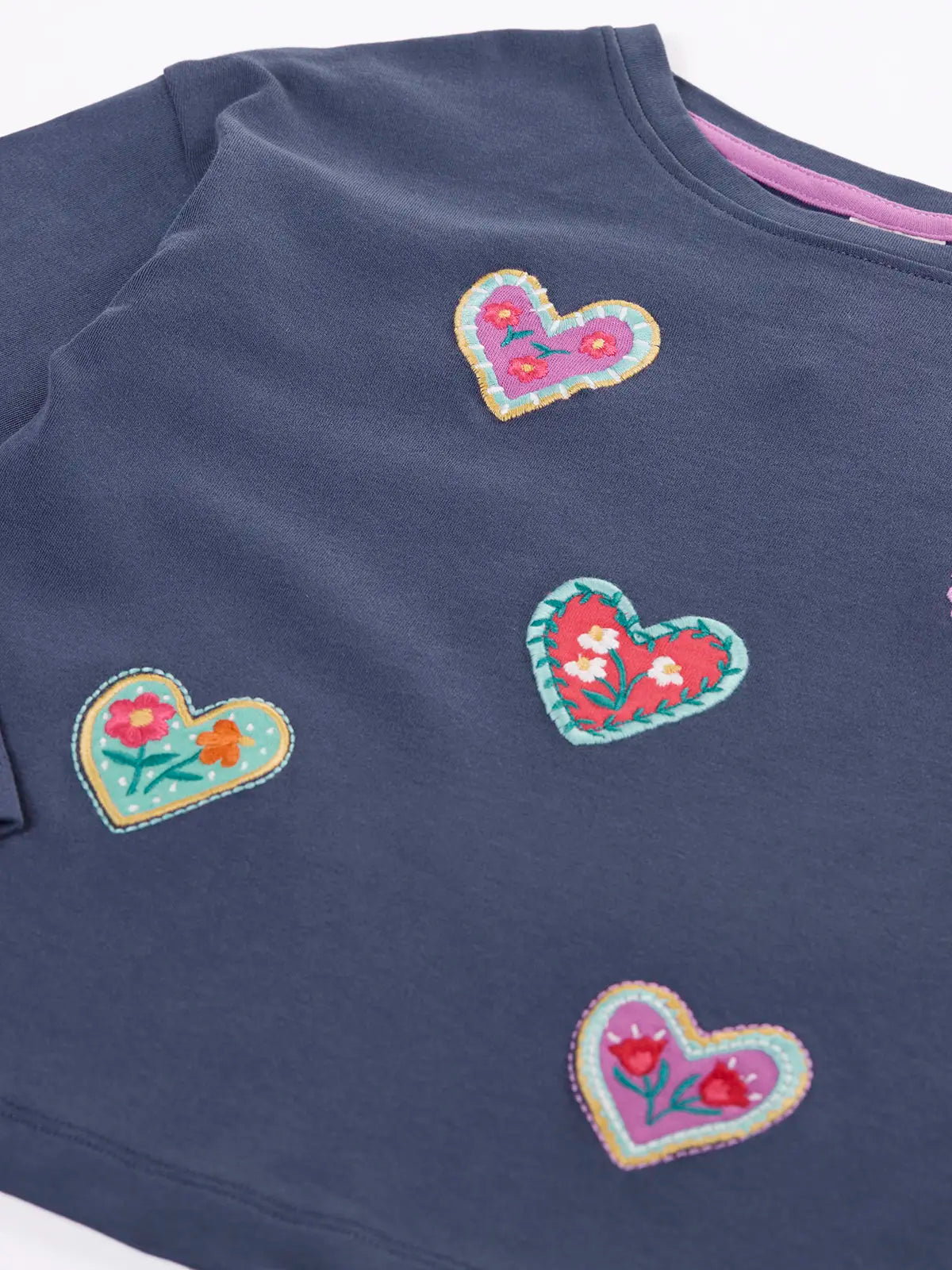 Close up Frugi bethany organic cotton long sleeved child's navy top with heart applies with floral embroidery details.
