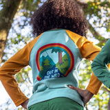 The back of a child in the woods, wearing the Frugi organic cotton long sleeved raglan top for kids, with an 'Out in the Wild' slogan and a colourful graphic on the back.