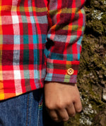 Child wearing Frugi organic cotton festive check hector long sleeve shirt with chest pocket. Close up of button on the sleeve cuffs.
