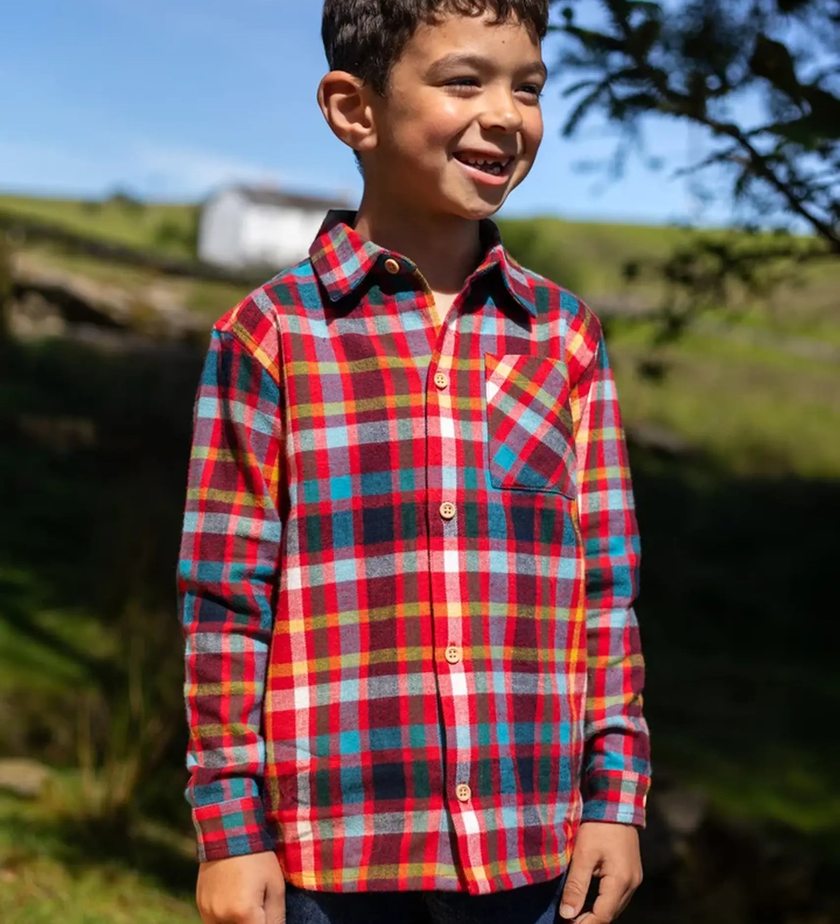 Child wearing the Frugi organic cotton festive check hector long sleeve shirt with chest pocket.