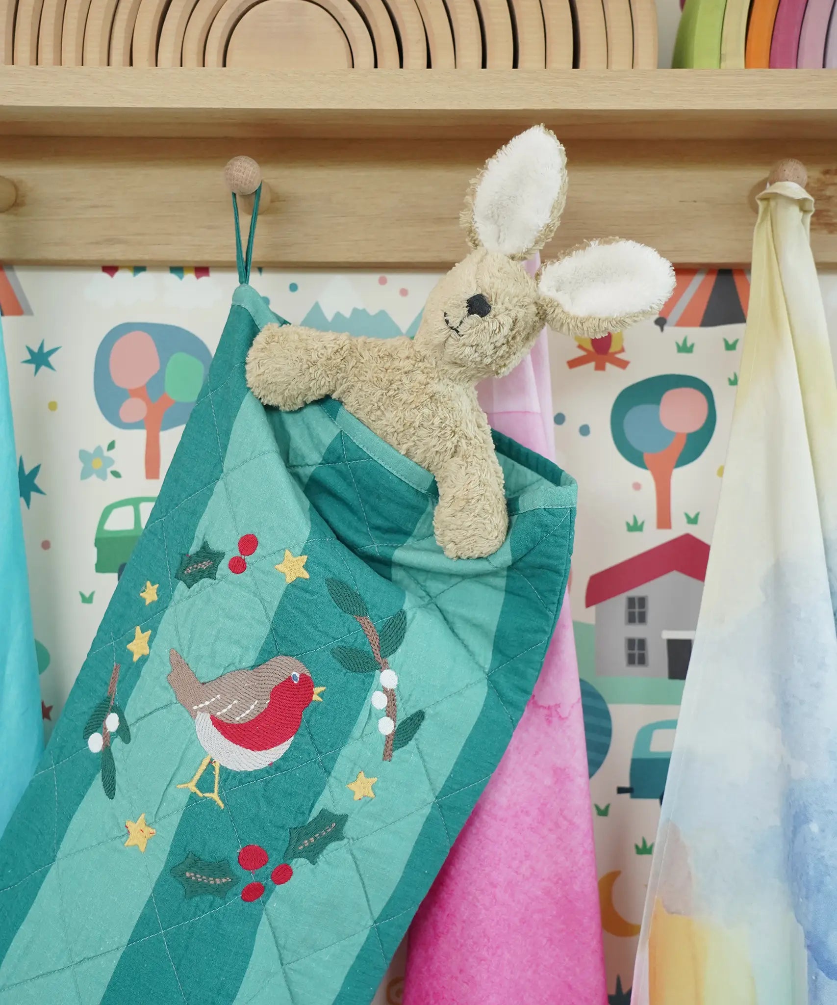Close up of Senger rabbit soft toy in the Frugi organic cotton Christmas stocking. Striped teal quilted style stocking with a robin wreath embroidery detail and hanging loop hung up in the Babipur playroom.