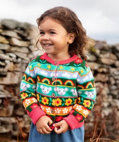 Child wearing the Frugi Robyn fairisle cardigan with a mouse Fair Isle design featuring flowers, rainbows, clouds and suns. 