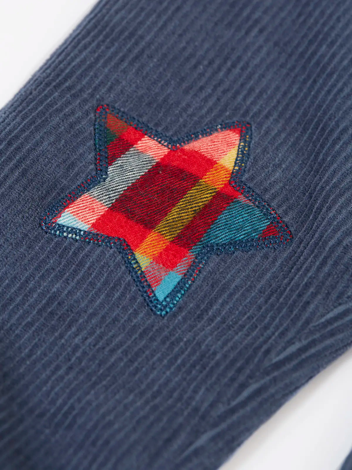 Close up of the festive check stars on the knees of the Frugi organic cotton ronnie reversible pull up trousers.
