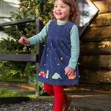 Child wearing the Frugi organic cotton rosalie reversible dress on the side in navy corduroy with festive appliques on the hemline with red tights underneath.