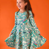 Child wearing the Frugi GOTS organic cotton sofia skater dress in polar aurora. Blue green background with and all over print featuring polar animals among star and colourful swishes. 