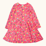 Frugi GOTS organic cotton sofia skater dress in fairy flutter. Pink background with colourful fairy print featuring flowers and leaves.