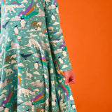 Close up of the side of the Frugi GOTS organic cotton sofia skater dress in polar aurora showing the flared skirt. Blue green background with and all over print featuring polar animals among star and colourful swishes. 